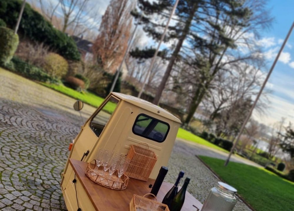 Piaggio Ape Bar von hinten in einem Park in Leverkusen, Gläser und Getränkespender auf der Holztheke